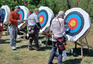4 archery bales with 3 people (2 men and 1 woman) scoring their arrows. 