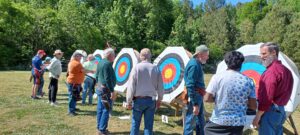 a line of 5 archery bales on a field with archers (men and women) standing before the bales and scoring their arrows