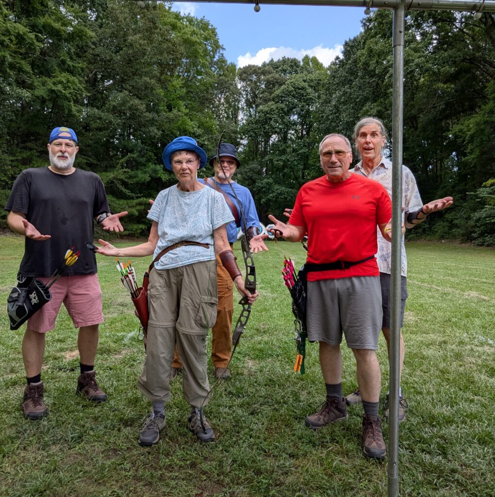 Five archers standing in a field, looking at the camera with (fake) expressions of shock and dismay.